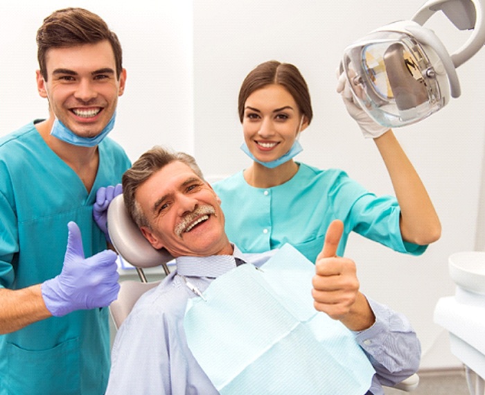 Patient smiling and giving thumbs up with dental team