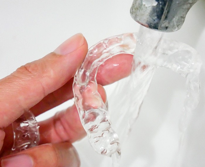 A person rinsing their Invisalign aligners under running water