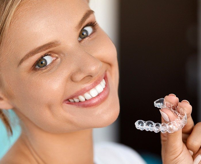 Smiling woman holding Invisalign clear aligner tray