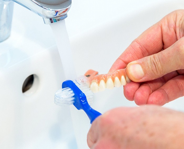 Patient cleaning dentures in sink