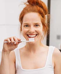 Woman brushing teeth to lower cost of dental emergencies in Gilbert