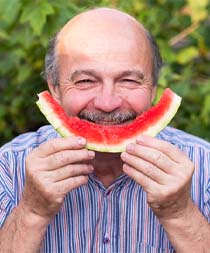 Smiling man eating watermelon to prevent dental emergencies in Gilbert