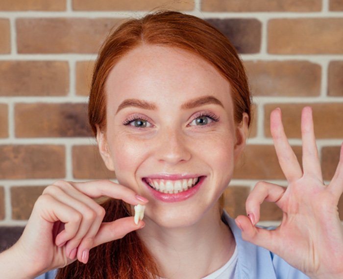 Red-haired woman holding up tooth after tooth extraction in Gilbert, AZ