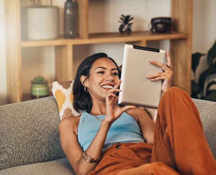 Smiling woman laying on couch while looking at tablet