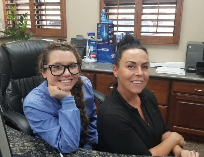 Two smiling Gilbert dental team members sitting at front desk