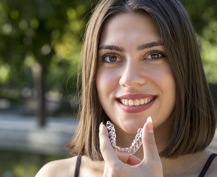A young girl smiling while holding a clear aligner in her hand as part of her Invisalign in Gilbert treatment