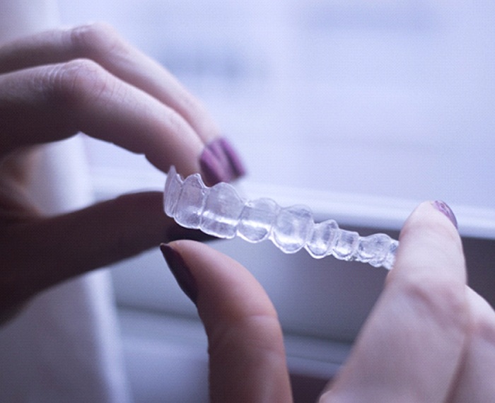 A person holding an Invisalign aligner between their fingers