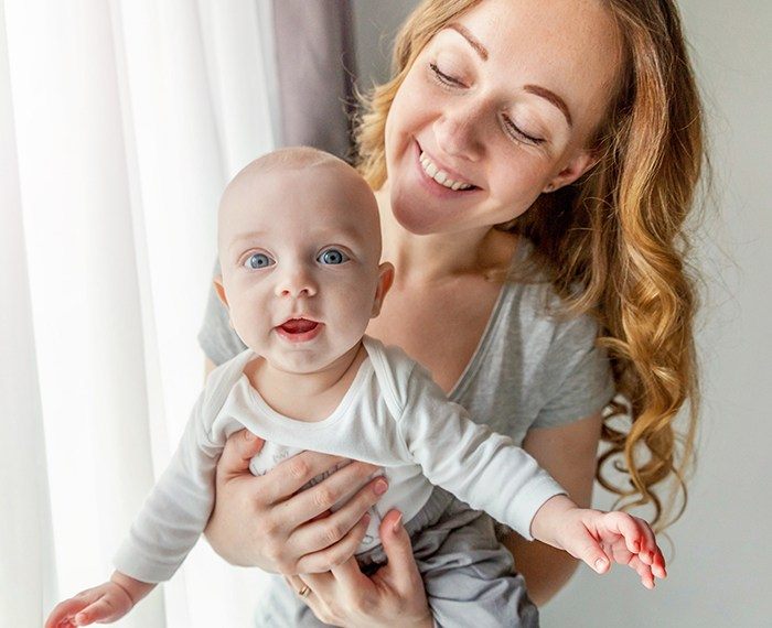 Mother holding smiling baby after frenectomy treatment for lip and tongue tie