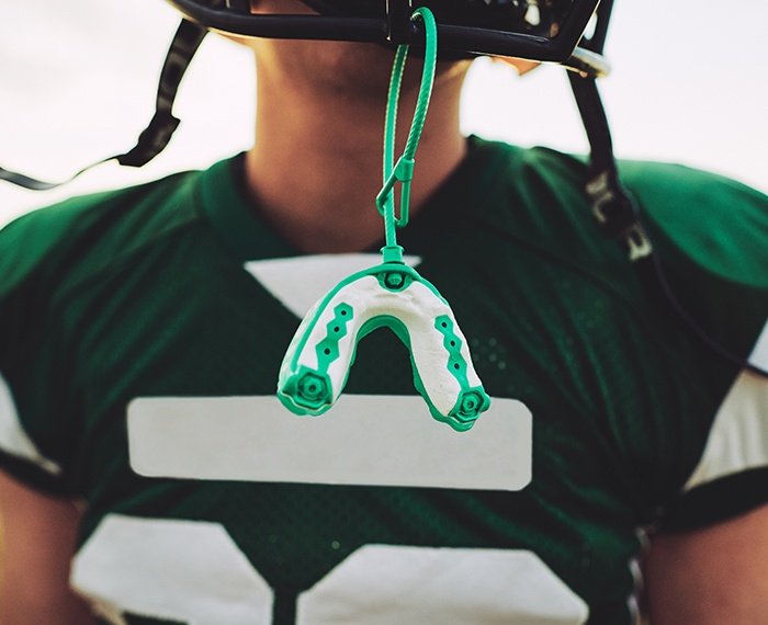 Teen with green athletic mouthguard hanging from football helmet