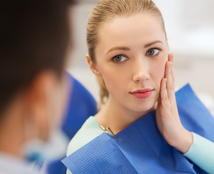 Woman holding her cheek in pain while talking to her dentist
