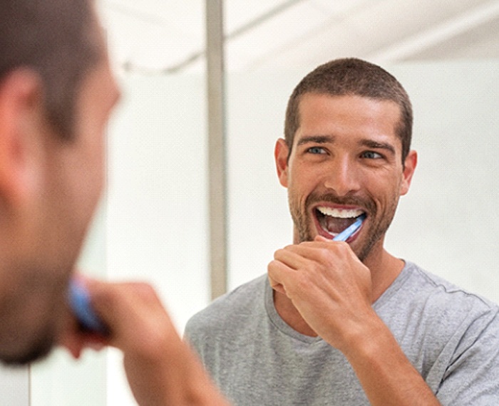 Man smiling while brushing his teeth