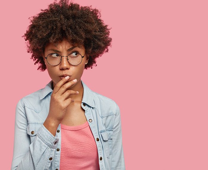 Woman wondering about veneers in Gilbert on pink background