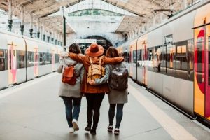 Three friends wearing backpacks walking through a train station together