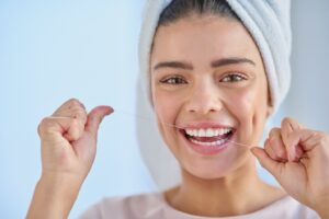 Woman wearing towel wrapped around her hair and flossing her teeth.